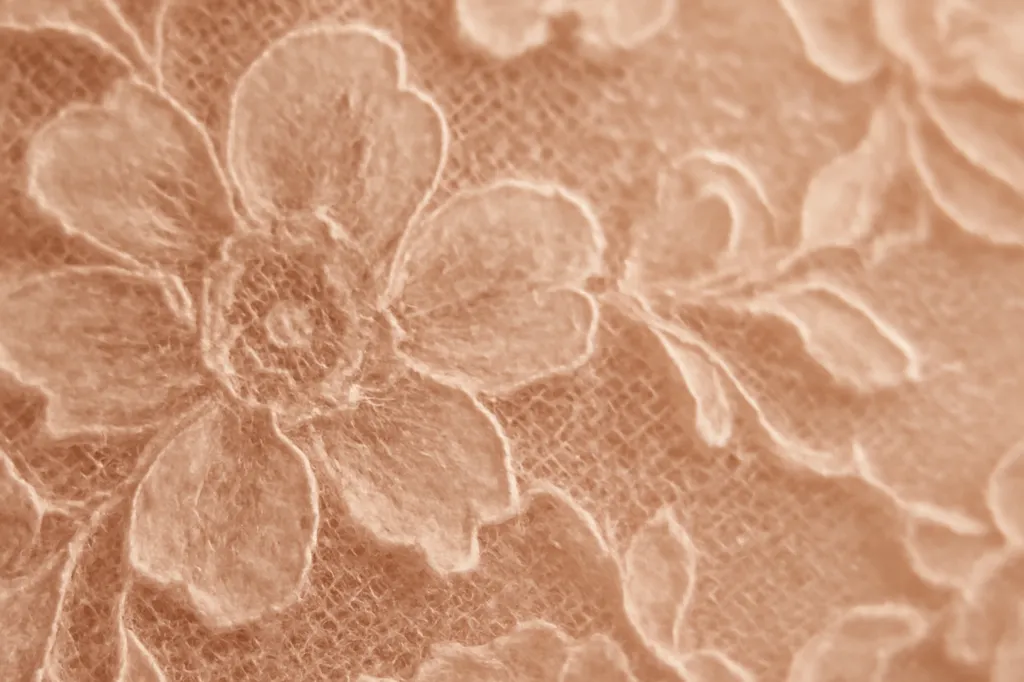 Gros plan sur une dentelle florale délicate en teinte blush, fils fins visibles